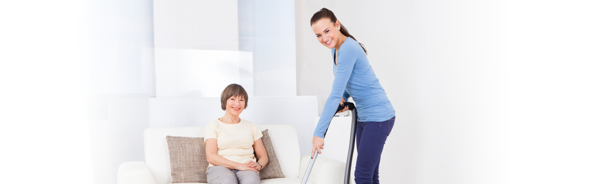 caregiver cleaning while elderly sits on a couch